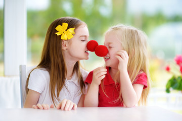 Happy little sisters wearing red clown noses having fun together on sunny summer day at home
