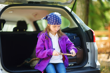 Cute little girl sitting in a car and using a pocket knife to whittle a hiking stick
