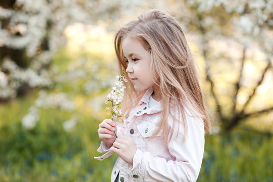 Stylish Kid Girl 4-5 Year Old Smelling Cherry Flowers Outdoors. Childhood.