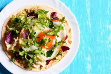 Fried egg, hummus and salad mix on flour tortilla. Delicious tortilla on a plate and on a blue background with copy space for text. Useful breakfast or lunch idea. Closeup