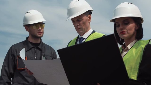 Goup of workers discuss blueprints using laptop outdoor on the solar farm