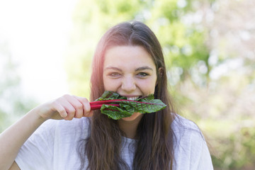 Portrait of a beautiful girl  looking at the camera biting a leaf of salad, backlit