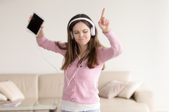 Young energetic woman listening to music using tablet wearing headphones, teenage girl dancing to good music in earphones at home, favorite song for meloman, music lover leisure