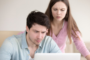 Fototapeta premium Unhappy couple using laptop, problems with connection, financial difficulties, broken computer. Serious anxious man and serious sad woman reading unpleasant e-mail letter or notification, bad news