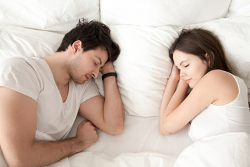 Young man and woman in white resting in bed at night, married couple sleeping peacefully together face to face, napping under blanket, guy wearing sleep tracking bracelet, high angle view