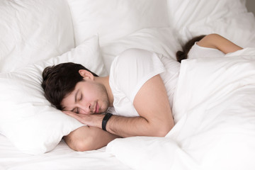 Obraz na płótnie Canvas Young guy and lady asleep together, having good dreams, healthy sleep, couple in bed taking a nap back to back. Sleeping man wearing smart wristband tracker for sleep tracking and getting up on time