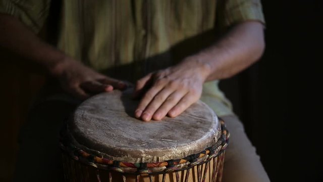 Closeup shot of man's hands drumming out a beat on an African skin-covered djembe hand drum.