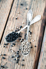 Mix of spices, peppercorns. Two metalic crossed teaspoons with black and white dried pepper grains on old vintage wooden table background. Top view.