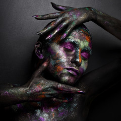 Young artistic woman in black paint and colourful powder. Glowing dark makeup. Creative body art on...