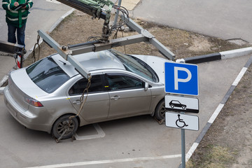 Tow truck loads  the car for violation of the parking rules. Fixing and lifting mechanism. Parking sign for disabled people