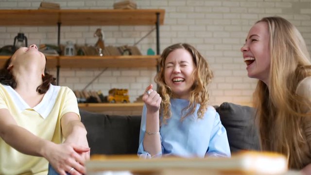 three young and energetic best friend girls talk together emotionally and lively with gestures and bright impression, laugh and smile while sitting on sofa at home during sunny day