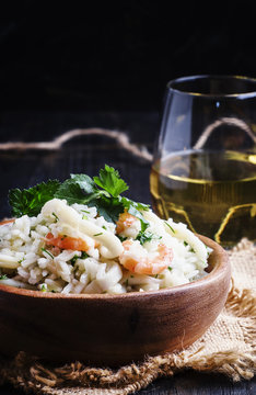 Risotto with shrimp and squid in a wooden bowl, dark background, selective focus