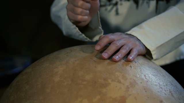 close up shot of man's hands drumming out a beat on an arabic percussion drum named Calabasse at home.
