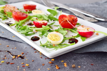 Fresh radish, cherry tomato, quail egg, ruccola with balsamic glaze on a white plate. Mediterranean lifestyle. Healthy food. Selective focus