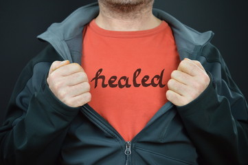 a man showing his t-shirt with the word healed on it