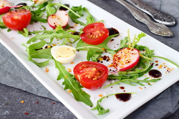 Fresh radish, cherry tomato, quail egg, ruccola with balsamic glaze on a white plate. Mediterranean lifestyle. Healthy food. Selective focus