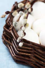 Easter decoration with blooming willow branches and colorful eggs in a basket on a blue fabric background