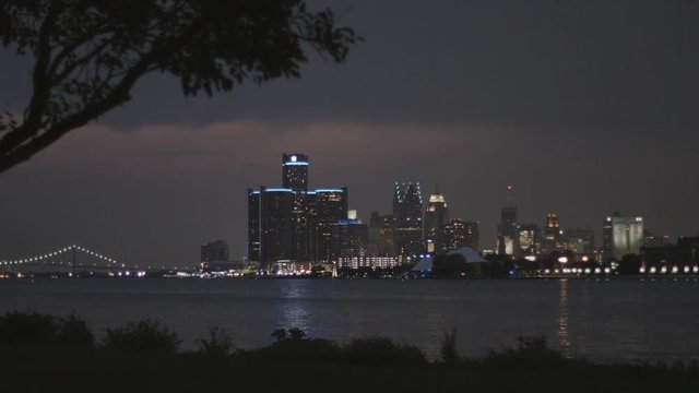 DETROIT, MI - CIRCA 2014: Establishing shot of the city skyline at night from Belle Isle looking across the Detroit River.  Close view with silhouetted foreground and overcast sky.