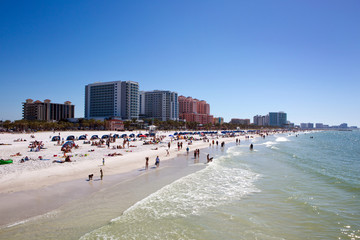 Tourists swim and play at the beach on Clearwater Beach, Florida with luxury hotels in the background.