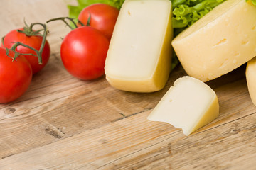 Cut cheese heads on wooden board served with tomatoes and fresh salad. Serving French homemade cheese. Food concept