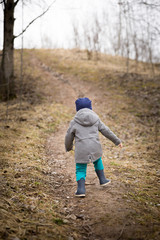 Back view on running little toddler. Child walking up the hill in the park on a spring or autumn day. Countryside lifestyle.