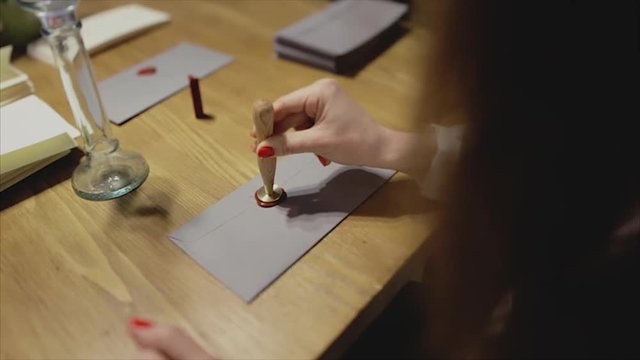 Girl put a seal with a sealing wax.Red wax seal or signet on lilac envelope.