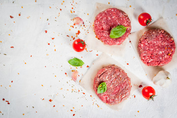 Fresh raw home-made minced beef steak burger with spices, tomatoes and basil, on a white stone concrete table, copy space, top view