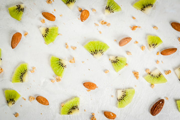 Food background. Ingredients for a healthy hearty breakfast, smoothies bowl, buddha bowl: fresh kiwi slices, almonds nuts, granola. On a white stone concrete table. Top view