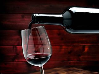 Red wine poured from a bottle in a elegant crystal goblet, on an antique wooden table.