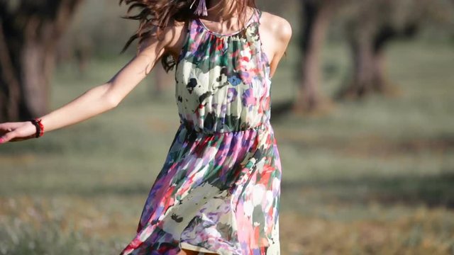 Giovane Ragazza con un vestito a fiori sta danzando allegramente in campagna tra il prato e gli alberi.