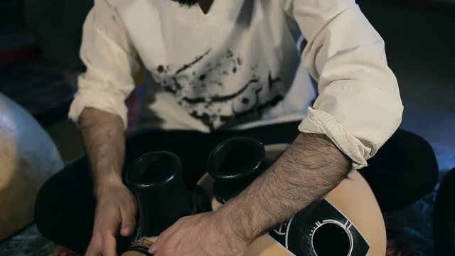 shot of man drumming out a beat on an arabic percussion drum named Frudu at home. Shot with other percussian drums on background.