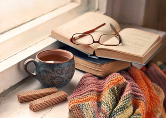 Cozy morning at home. A cup of tea, a blanket, old books and glasses on the windowsill, selective...