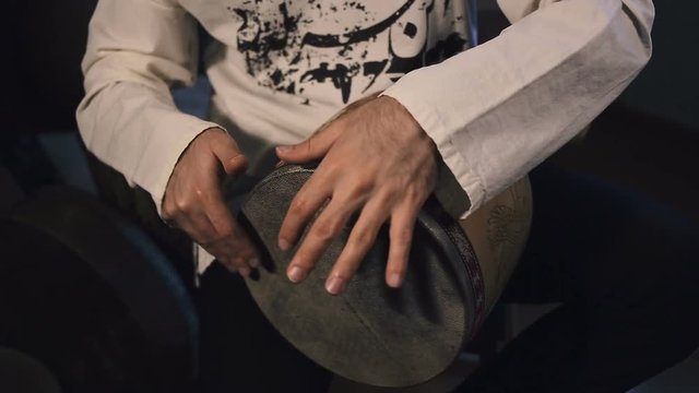 panoramic shot of man's hands drumming out a beat on an arabic percussion drum named Tombak at home. Shot with other percussian drums on background.