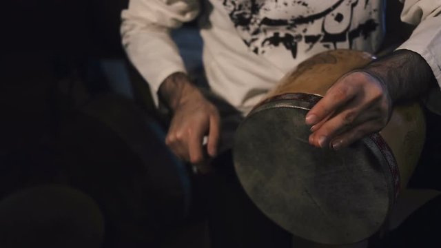 shot of man's hands drumming out a beat on an arabic percussion drum named Tombak at home. Shot on dark background.