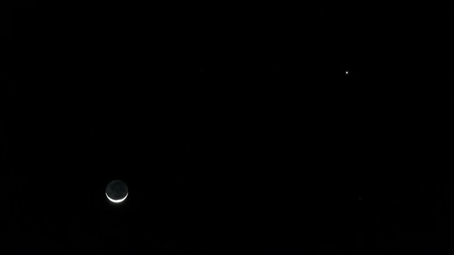 Static timelapse of a sickle moon setting against a dark and contrasty night sky.