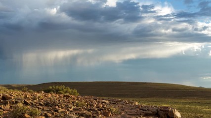 A slow panning timelapse of a vast open landscape with rocky foreground while following stormy clouds and rain falling against a dark, dramatic sky - Powered by Adobe