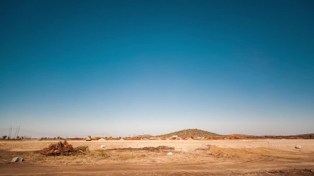 Static pan timelapse of a construction site on a mine while earthworks is in progress with heavy load machinery, trucks and tippers close to action