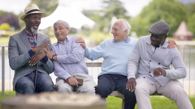  Portrait happy multiracial senior friends relaxing & chatting in the park