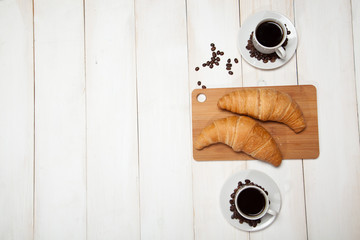 Cups of coffee and a croissants on a white wooden table