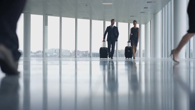  Business people traveling walking thru large open plan building with luggage