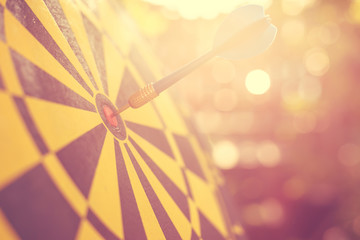 Blue dart arrow in the center of dartboard. Blur and bokeh in sunrise time background. Warm vintage effect style