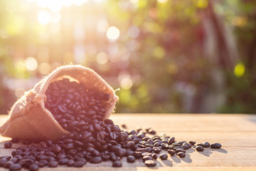 Roasted coffee beans in small sack on wooden table. Outdoor shooting with sunlight and blur background