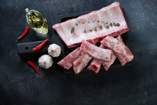 Raw sliced pork ribs on a black wooden serving board, top view on a dark metal background, horizontal shot