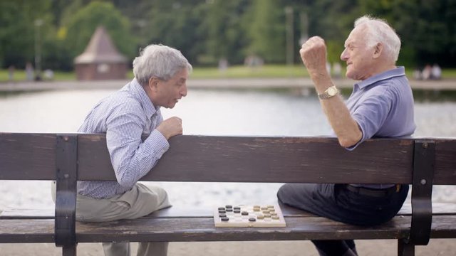  Happy senior male friends playing draughts in the park