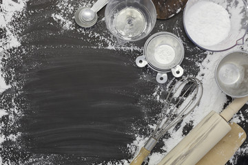 flour sprinkled with different kitchen tools on dark black background. Baking ingredient Top view.