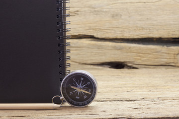 Compass with notebook and pencil on old wooden background.