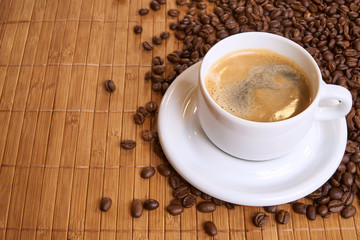 A cup of black coffee on bamboo surrounded by coffee beans with copyspace