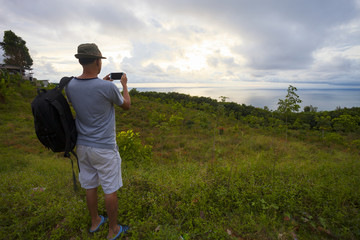 Traveler man with backpacker standing take a photo landscape tropical sea view sunset andaman sea.