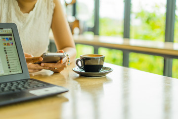 Women's hands holding smartphone with coffee on notebook place