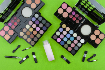 Flat lay photo of various makeup brush, eyeshadow and cosmetics on colorful paper background.